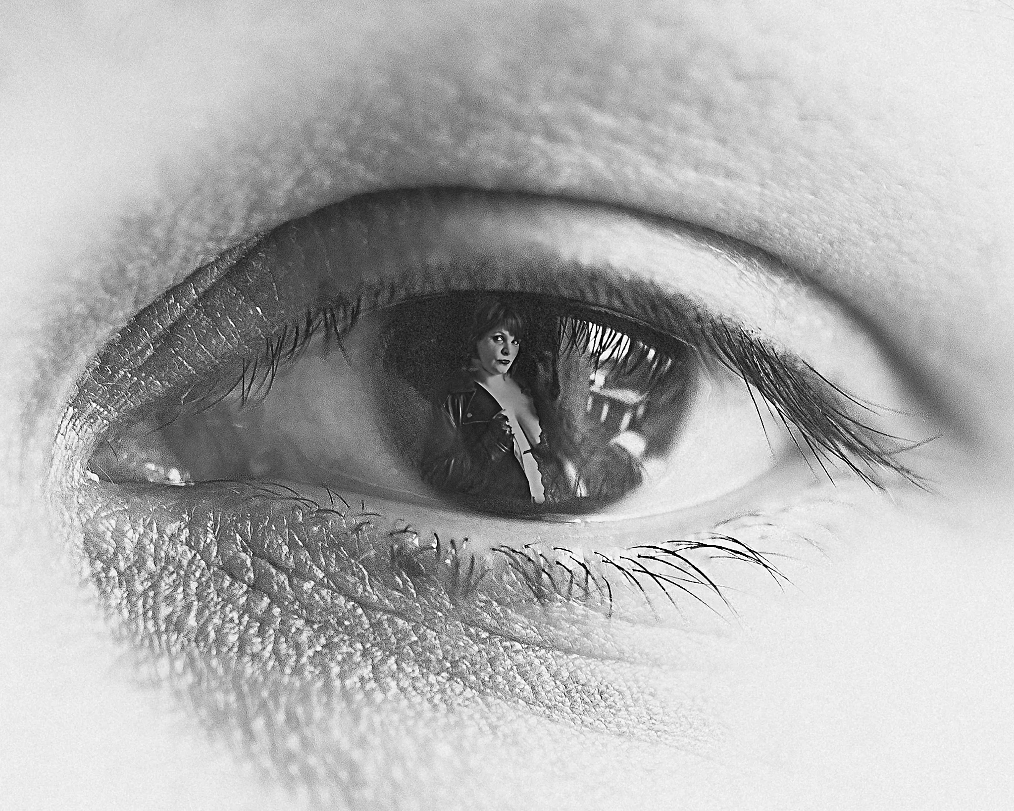 Creative - Schwarzweiße Detailaufnahme eines Auges in extremer Nahaufnahme; in der Iris spiegelt sich eine Frau in Dessous und Jacke, wodurch eine doppelte Bildebene entsteht, während die feinen Hautstrukturen und Wimpern durch das weiche Licht betont werden und eine ruhige, zugleich geheimnisvolle und konzeptionelle Bildwirkung erzeugen.